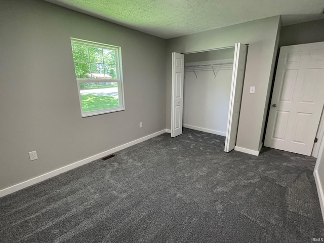 unfurnished bedroom with a textured ceiling, dark colored carpet, and a closet