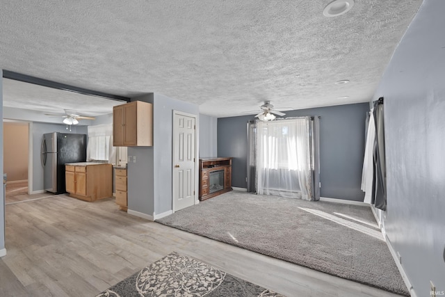 unfurnished living room featuring light hardwood / wood-style flooring, a textured ceiling, and ceiling fan