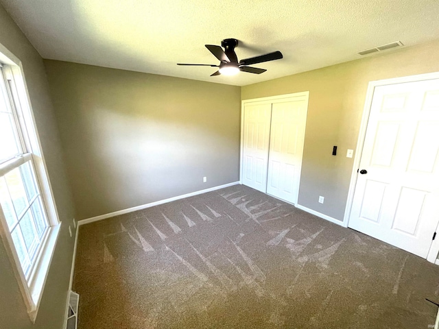 unfurnished bedroom with ceiling fan, a textured ceiling, and dark carpet