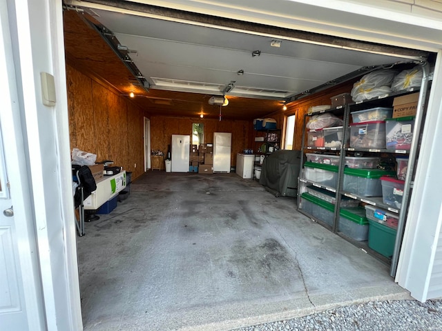 garage with a garage door opener, wood walls, and white refrigerator