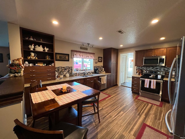 kitchen featuring backsplash, stainless steel appliances, a textured ceiling, wood-type flooring, and sink