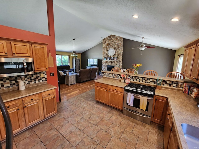 kitchen with decorative backsplash, a fireplace, stainless steel appliances, lofted ceiling, and ceiling fan