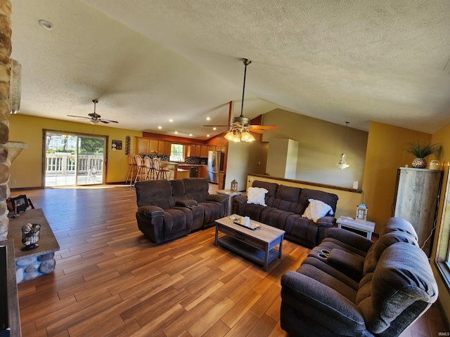 living room with wood-type flooring, a textured ceiling, vaulted ceiling, and ceiling fan