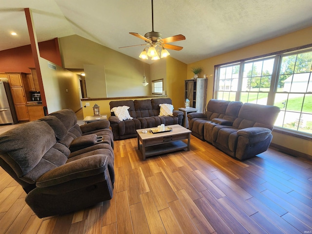 living room with a textured ceiling, vaulted ceiling, ceiling fan, and light hardwood / wood-style flooring