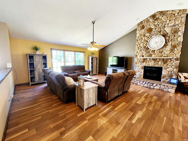 living room featuring ceiling fan, a stone fireplace, hardwood / wood-style flooring, and vaulted ceiling