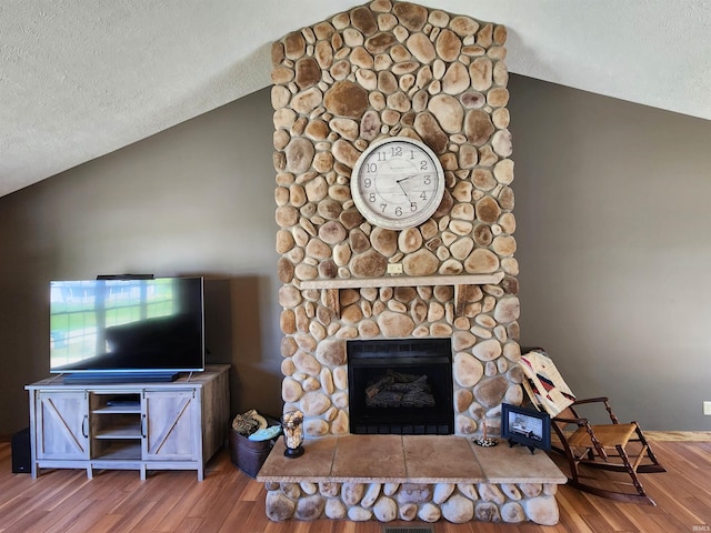 unfurnished living room featuring a stone fireplace, hardwood / wood-style flooring, and lofted ceiling