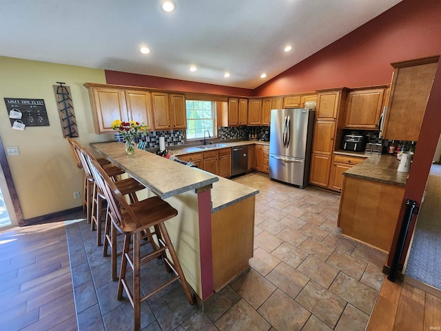 kitchen with vaulted ceiling, kitchen peninsula, a kitchen breakfast bar, stainless steel appliances, and backsplash