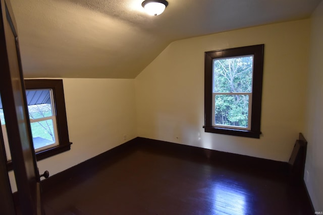 bonus room with a textured ceiling, vaulted ceiling, and dark wood-type flooring