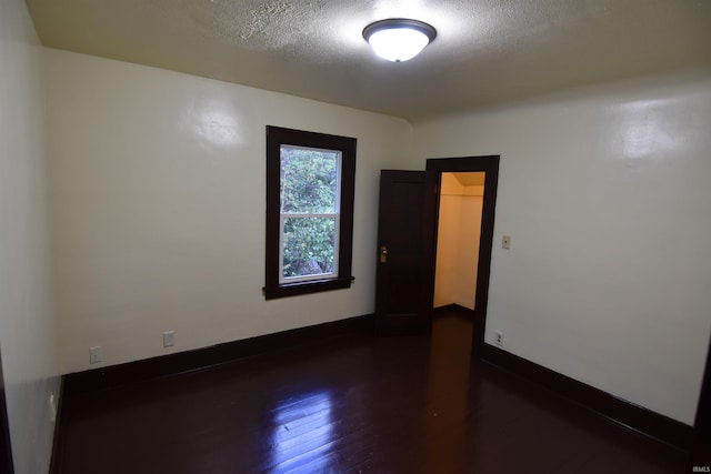 empty room with a textured ceiling and dark hardwood / wood-style flooring