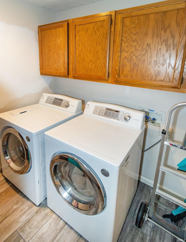 clothes washing area with cabinets, a textured ceiling, washing machine and clothes dryer, and light hardwood / wood-style floors