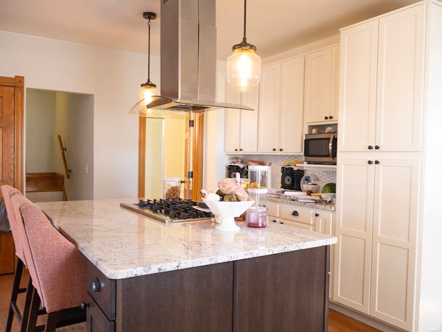 kitchen with hanging light fixtures, white cabinetry, light stone countertops, stainless steel appliances, and island exhaust hood