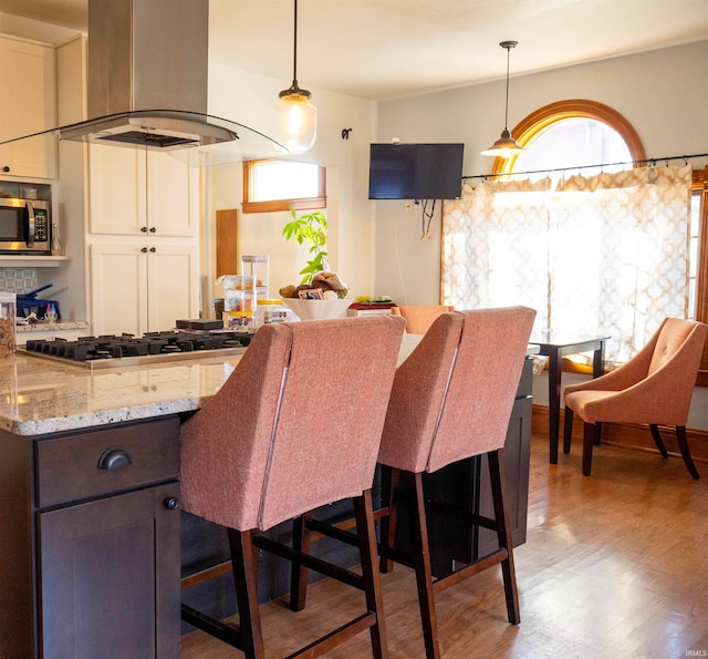 kitchen featuring white cabinets, island exhaust hood, stainless steel appliances, light stone countertops, and hardwood / wood-style floors