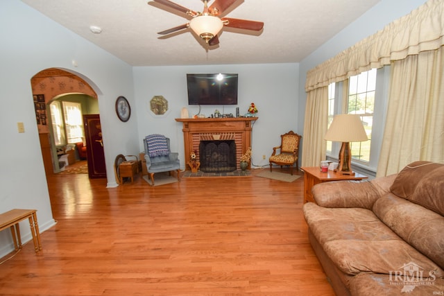 living room featuring a brick fireplace, light hardwood / wood-style floors, and ceiling fan