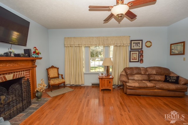 living room featuring a textured ceiling, wood-type flooring, a fireplace, and ceiling fan