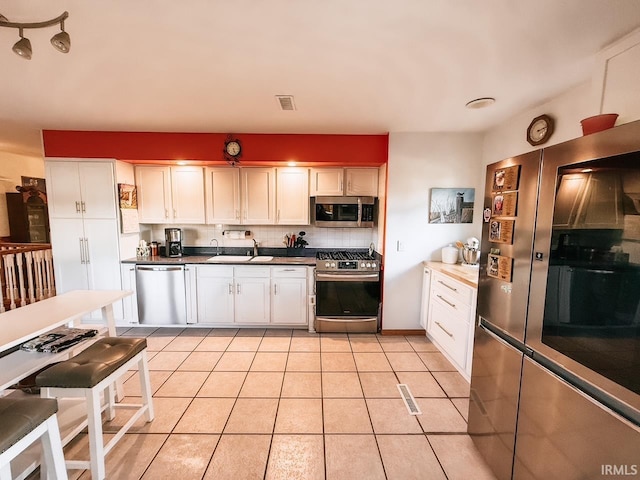 kitchen featuring light tile patterned floors, sink, white cabinetry, appliances with stainless steel finishes, and decorative backsplash