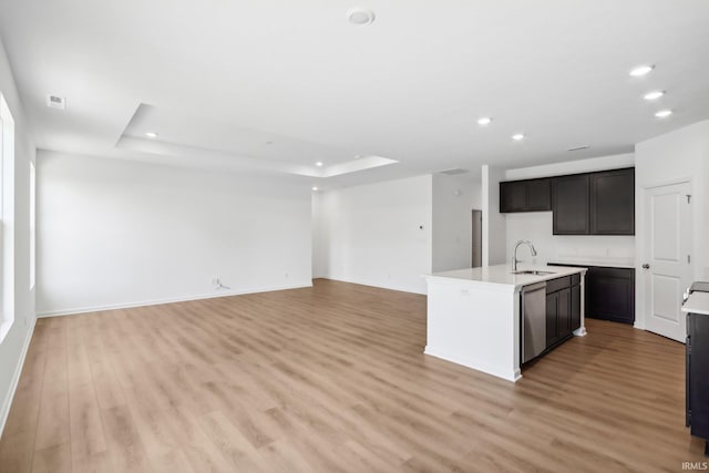 kitchen featuring dishwasher, sink, light wood-type flooring, an island with sink, and a tray ceiling