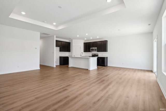 unfurnished living room with a tray ceiling, light hardwood / wood-style flooring, and sink