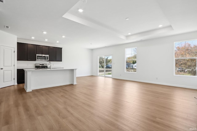 unfurnished living room featuring a raised ceiling, sink, and light hardwood / wood-style flooring