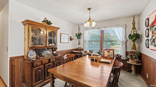 carpeted dining space with a textured ceiling, wooden walls, and an inviting chandelier