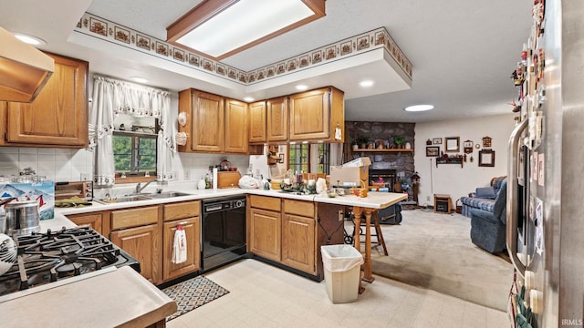 kitchen with black dishwasher, kitchen peninsula, light colored carpet, exhaust hood, and a stone fireplace