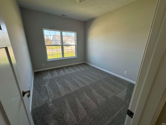 unfurnished room with a textured ceiling and dark colored carpet