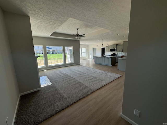 unfurnished living room featuring a textured ceiling, wood-type flooring, ceiling fan, and a raised ceiling