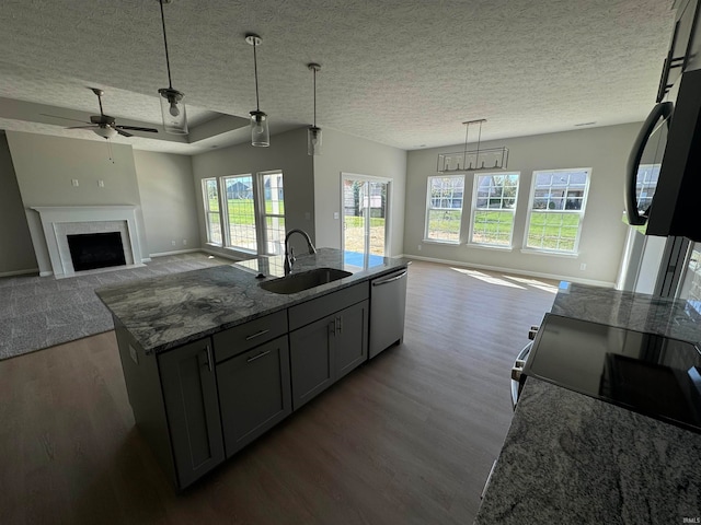 kitchen featuring gray cabinets, a kitchen island with sink, sink, dark stone countertops, and stainless steel dishwasher