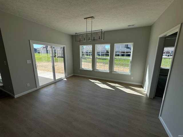 unfurnished dining area with an inviting chandelier, a textured ceiling, dark hardwood / wood-style floors, and a wealth of natural light