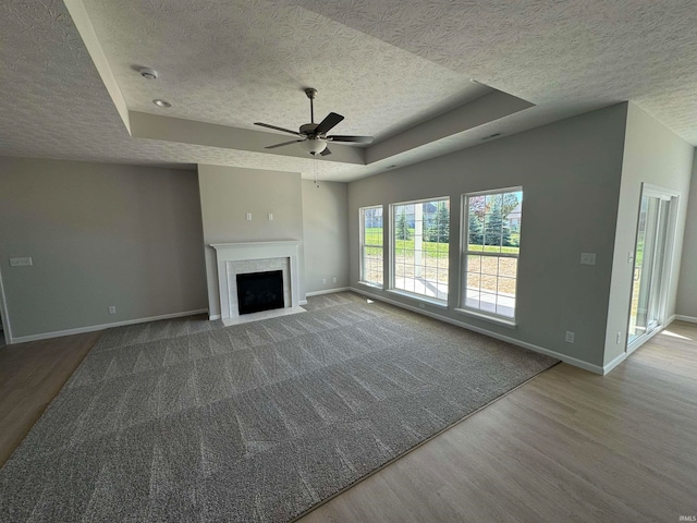 unfurnished living room with ceiling fan, a textured ceiling, a raised ceiling, and hardwood / wood-style floors