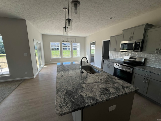 kitchen with sink, an island with sink, gray cabinetry, appliances with stainless steel finishes, and decorative light fixtures