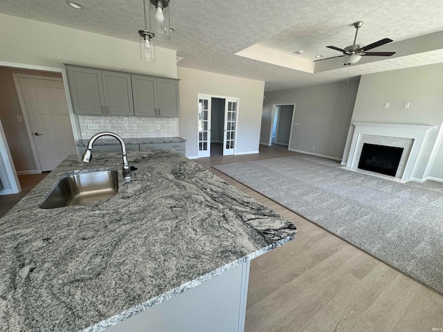 kitchen featuring gray cabinetry, light hardwood / wood-style floors, light stone counters, backsplash, and sink