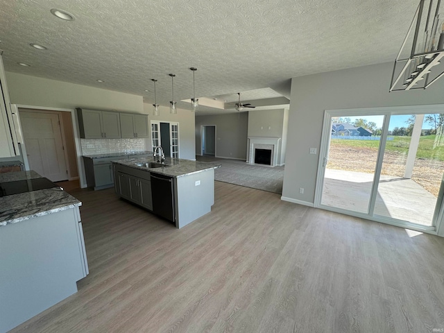 kitchen featuring dishwasher, a kitchen island with sink, hanging light fixtures, gray cabinetry, and light hardwood / wood-style flooring