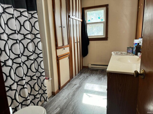 bathroom featuring a baseboard heating unit, curtained shower, vanity, and toilet