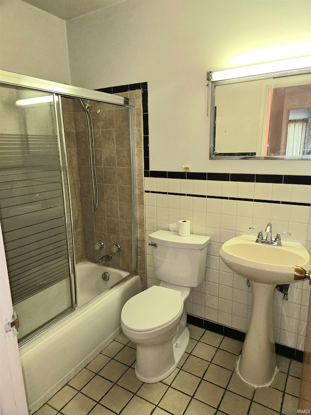 full bathroom with tile walls, tile patterned flooring, bath / shower combo with glass door, and toilet