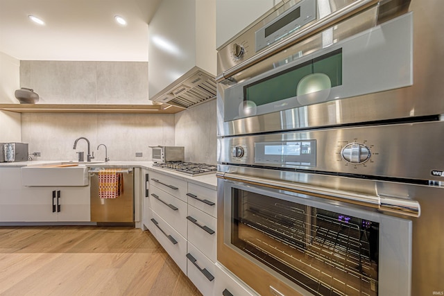 kitchen featuring appliances with stainless steel finishes, island range hood, white cabinetry, and light hardwood / wood-style flooring