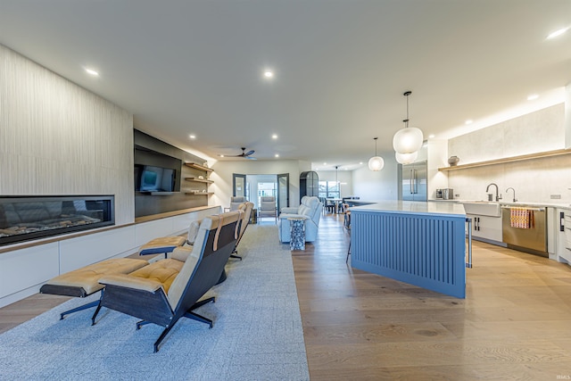 kitchen featuring hanging light fixtures, a kitchen island, dishwasher, a fireplace, and light wood-type flooring