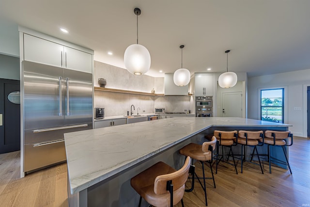 kitchen with stainless steel appliances, light hardwood / wood-style floors, hanging light fixtures, and a spacious island