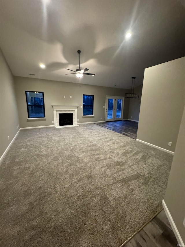 unfurnished living room with ceiling fan, a brick fireplace, and dark colored carpet