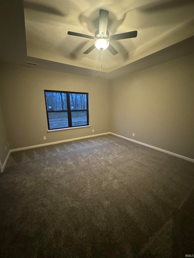 carpeted empty room with a raised ceiling and ceiling fan