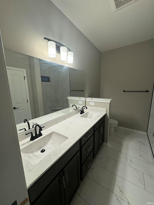 bathroom with a tile shower, vanity, toilet, and a textured ceiling