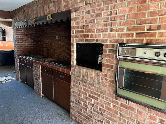 kitchen with dark brown cabinetry, carpet floors, brick wall, and black appliances