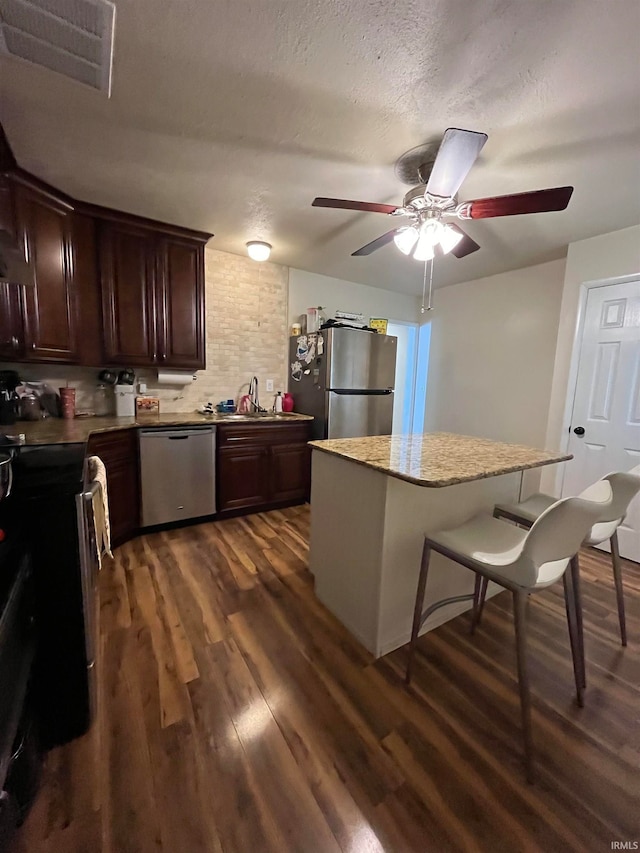 kitchen featuring dark hardwood / wood-style flooring, dark brown cabinets, stainless steel appliances, a kitchen bar, and a center island