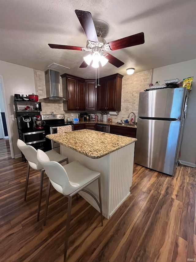 kitchen featuring light stone counters, a textured ceiling, wall chimney exhaust hood, appliances with stainless steel finishes, and dark hardwood / wood-style flooring