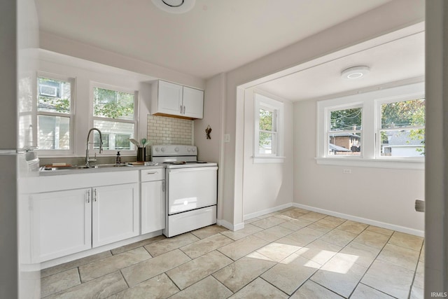 kitchen featuring white range, backsplash, a healthy amount of sunlight, and white cabinetry