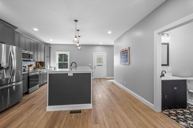 kitchen with tasteful backsplash, sink, light hardwood / wood-style flooring, appliances with stainless steel finishes, and a center island with sink