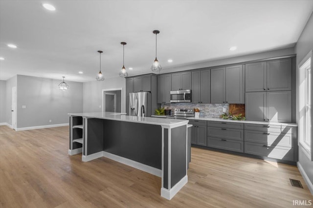 kitchen featuring decorative light fixtures, a kitchen island with sink, gray cabinets, stainless steel appliances, and light wood-type flooring