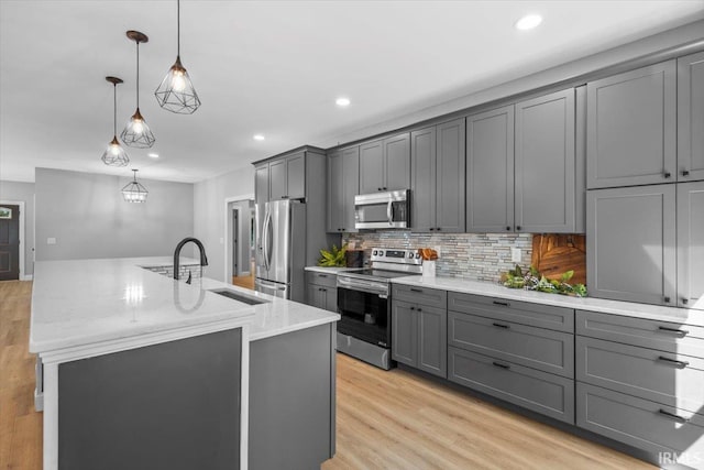 kitchen featuring gray cabinetry, hanging light fixtures, light hardwood / wood-style flooring, appliances with stainless steel finishes, and a center island with sink