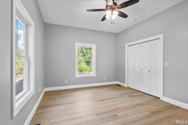 unfurnished bedroom with ceiling fan, a closet, light hardwood / wood-style floors, and multiple windows