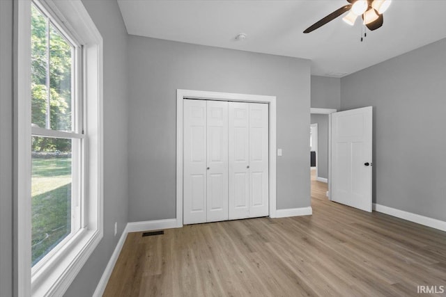 unfurnished bedroom featuring light wood-type flooring, multiple windows, ceiling fan, and a closet