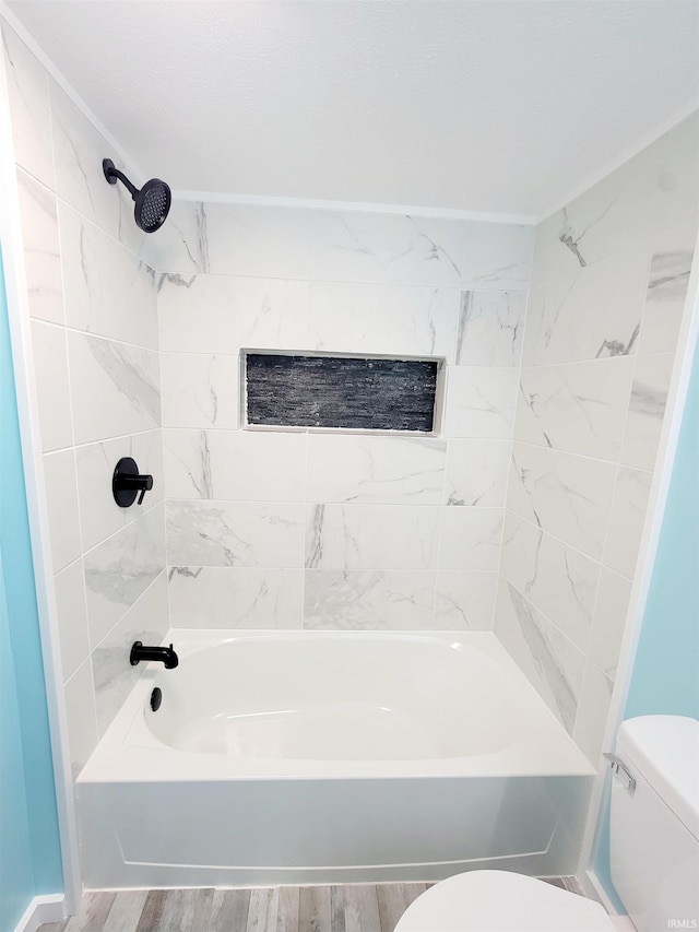 bathroom with wood-type flooring, tiled shower / bath, and toilet